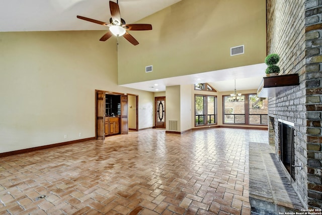 unfurnished living room with ceiling fan with notable chandelier, a high ceiling, and a brick fireplace