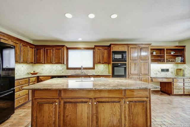 kitchen with black appliances, light stone countertops, a kitchen island, sink, and tasteful backsplash