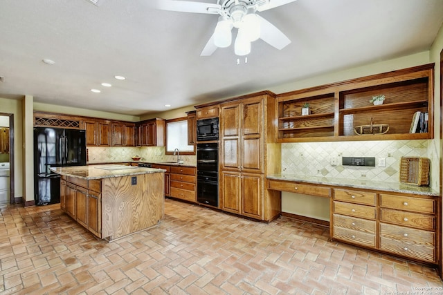 kitchen featuring built in desk, backsplash, light stone countertops, a kitchen island, and black appliances