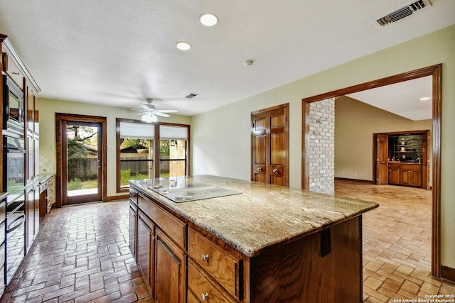 kitchen with a center island, light stone counters, ceiling fan, black electric stovetop, and stainless steel microwave