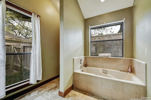 bathroom with lofted ceiling, tile patterned flooring, a relaxing tiled tub, and a healthy amount of sunlight