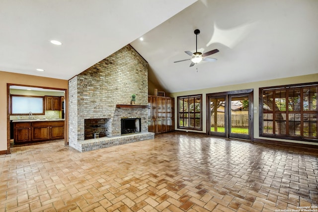 unfurnished living room with a brick fireplace, high vaulted ceiling, ceiling fan, and sink