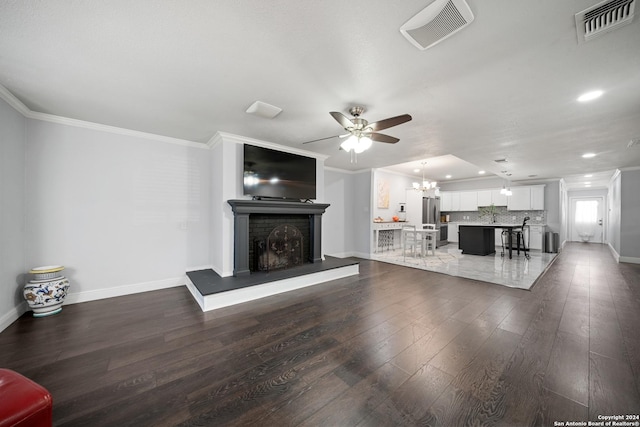 unfurnished living room featuring ceiling fan with notable chandelier, crown molding, and dark wood-type flooring