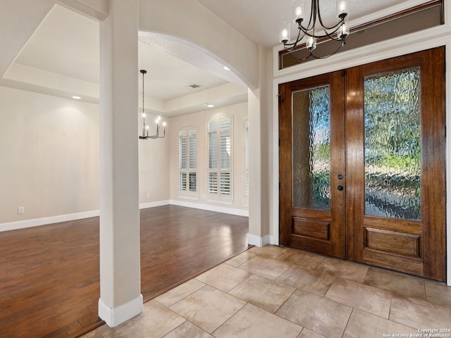 tiled entryway featuring a chandelier, a raised ceiling, and french doors