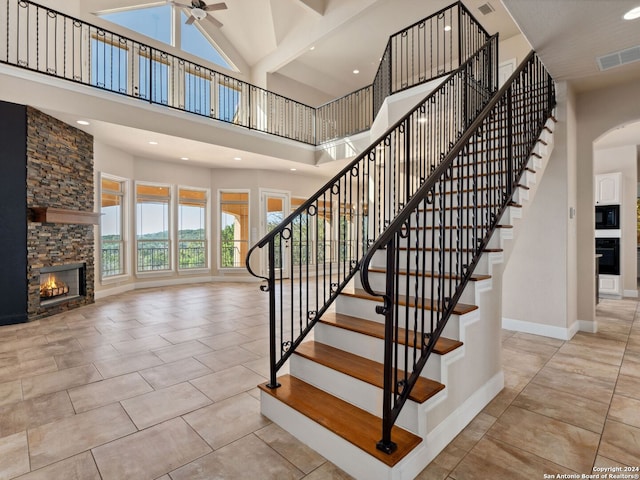 stairs with a stone fireplace, ceiling fan, and a towering ceiling