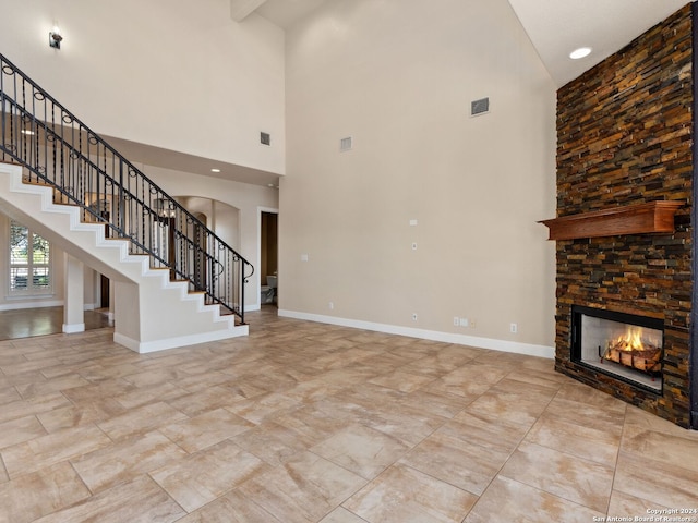 unfurnished living room featuring a stone fireplace and a towering ceiling