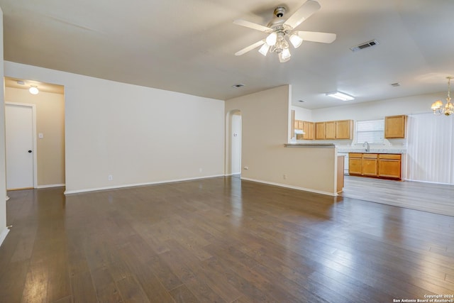 unfurnished living room featuring dark hardwood / wood-style flooring, ceiling fan with notable chandelier, and sink