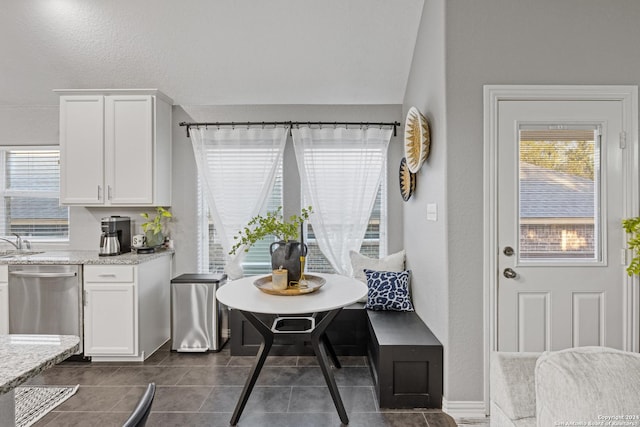 kitchen with light stone countertops, white cabinets, dark tile patterned floors, sink, and dishwasher