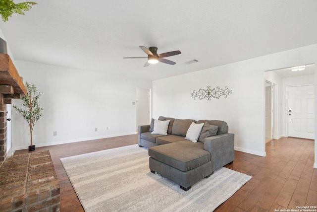 living room with ceiling fan, wood-type flooring, and a brick fireplace