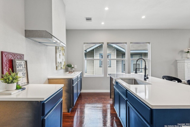 kitchen with wall chimney exhaust hood, dark hardwood / wood-style floors, blue cabinets, and sink