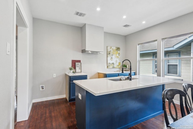 kitchen featuring sink, dark wood-type flooring, blue cabinets, an island with sink, and a breakfast bar