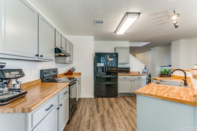 kitchen featuring sink, black appliances, light wood-type flooring, and wooden counters