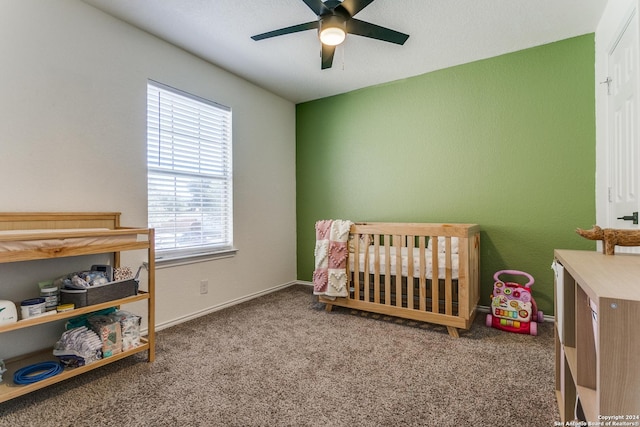 carpeted bedroom featuring ceiling fan and a nursery area