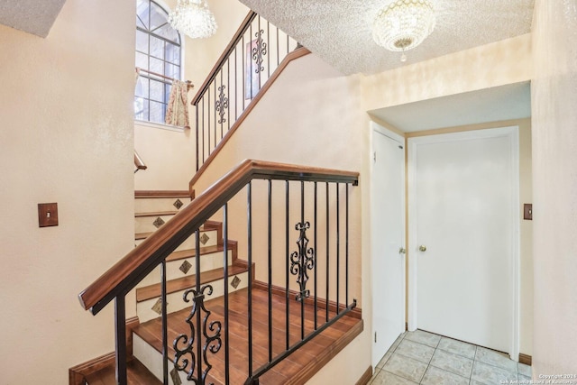 staircase with tile patterned flooring, a textured ceiling, and an inviting chandelier