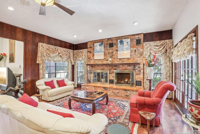 living room featuring hardwood / wood-style flooring, a textured ceiling, wooden walls, and a brick fireplace