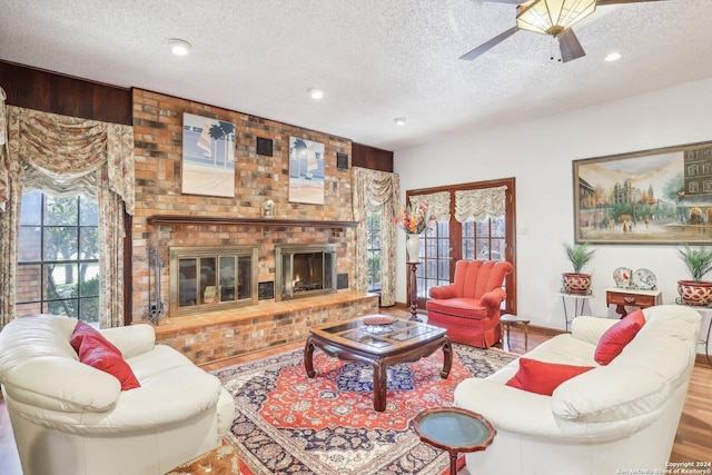 living room featuring ceiling fan, a fireplace, hardwood / wood-style floors, and a textured ceiling