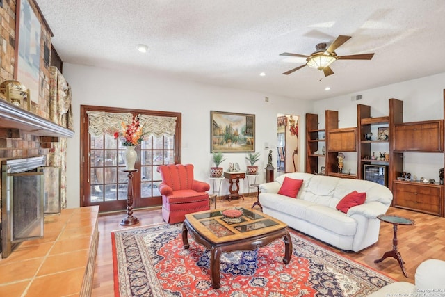 living room with a brick fireplace, a textured ceiling, light hardwood / wood-style flooring, and ceiling fan