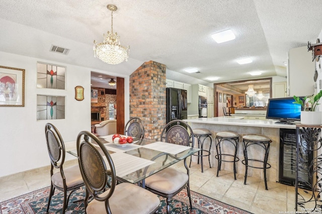 dining space with wine cooler, a fireplace, ceiling fan with notable chandelier, and a textured ceiling