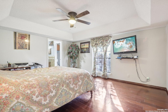 bedroom featuring ensuite bath, ceiling fan, a textured ceiling, a tray ceiling, and dark hardwood / wood-style flooring