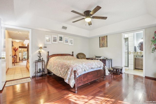 bedroom featuring wood-type flooring, a raised ceiling, ensuite bath, and ceiling fan