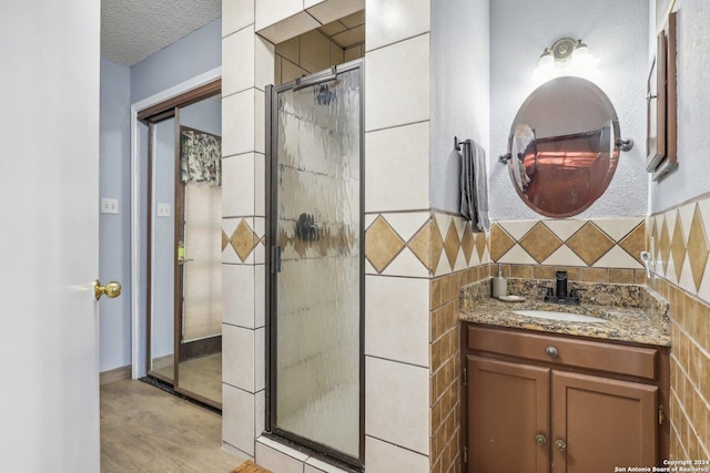 bathroom featuring a textured ceiling, vanity, tile walls, and walk in shower