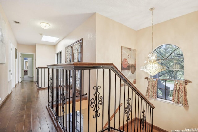 hall with a textured ceiling, a chandelier, dark wood-type flooring, and a skylight