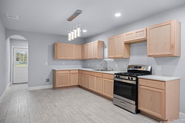 kitchen with light brown cabinetry, stainless steel gas range oven, sink, an inviting chandelier, and light hardwood / wood-style floors