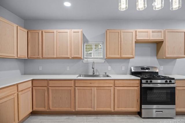 kitchen featuring gas stove, light brown cabinetry, sink, and hanging light fixtures