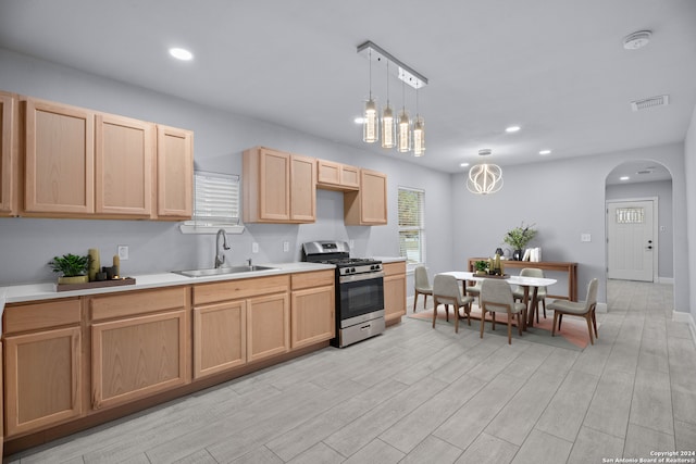 kitchen featuring sink, hanging light fixtures, a notable chandelier, stainless steel range with gas stovetop, and light wood-type flooring