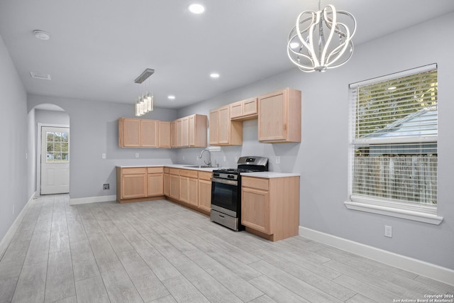 kitchen with light brown cabinetry, light wood-type flooring, a notable chandelier, and stainless steel gas range