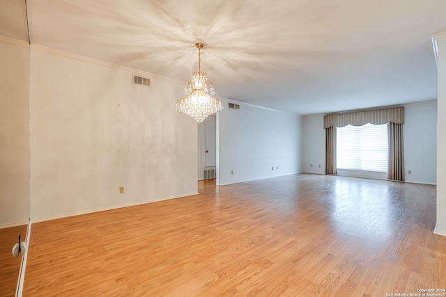 spare room featuring crown molding, light hardwood / wood-style flooring, and an inviting chandelier