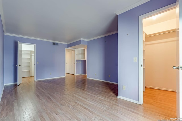 unfurnished bedroom featuring light wood-type flooring, a spacious closet, crown molding, and a closet