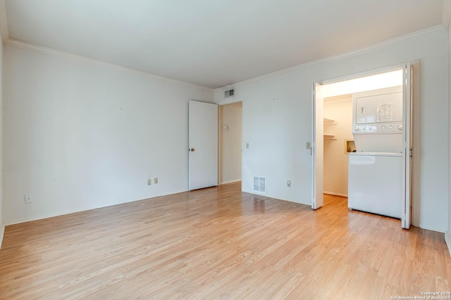 spare room featuring light wood-type flooring, stacked washer / dryer, and ornamental molding