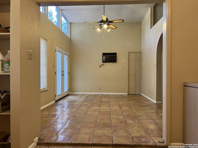 entryway featuring ceiling fan, a wall mounted air conditioner, a towering ceiling, a textured ceiling, and light tile patterned floors