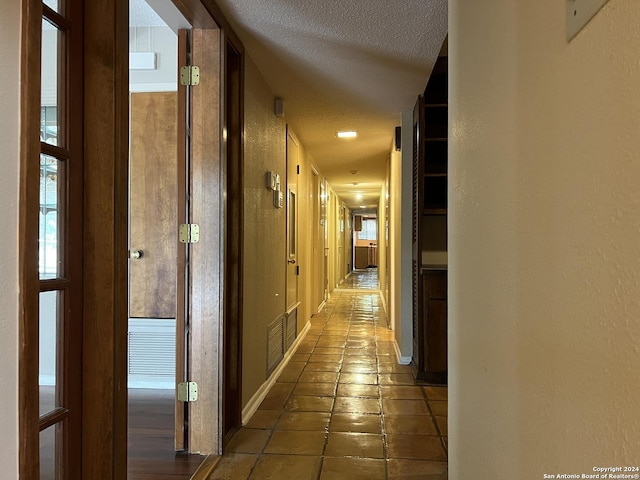 corridor with a textured ceiling and dark tile patterned floors