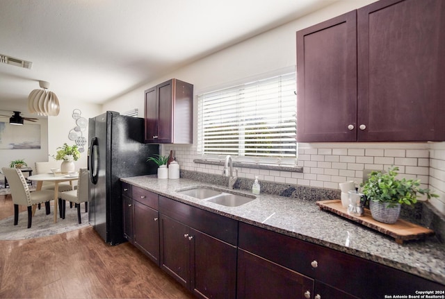 kitchen with decorative backsplash, black fridge, light stone counters, sink, and hardwood / wood-style floors