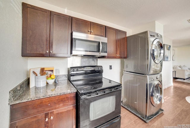 kitchen featuring light wood-type flooring, black range with electric stovetop, dark stone counters, and stacked washer and clothes dryer