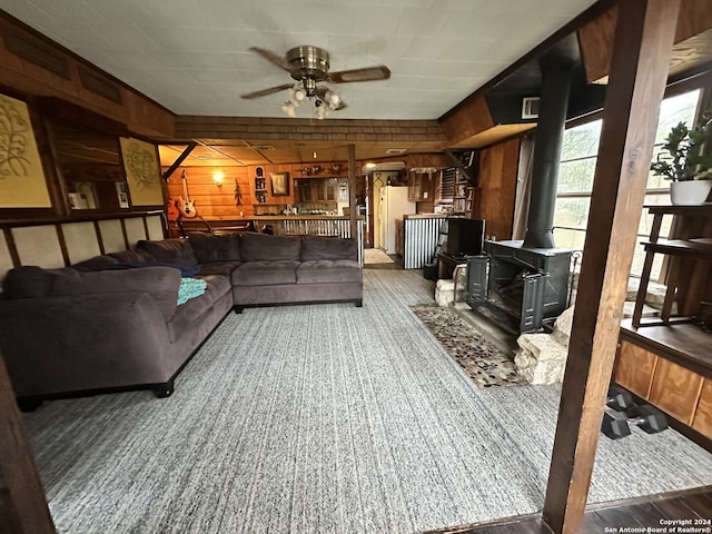 living room with a wood stove, ceiling fan, and wood walls