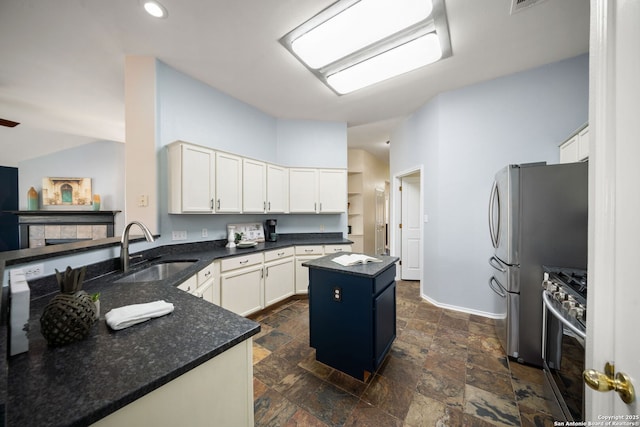 kitchen with white cabinets, appliances with stainless steel finishes, a center island, dark stone countertops, and sink