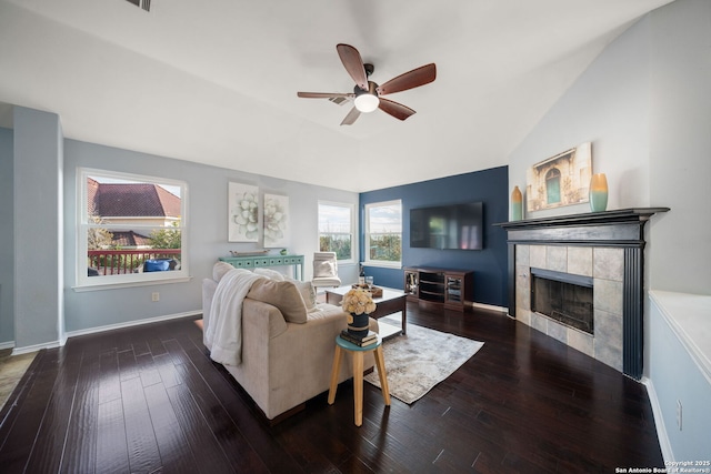 living room featuring dark hardwood / wood-style floors, lofted ceiling, a tiled fireplace, and ceiling fan