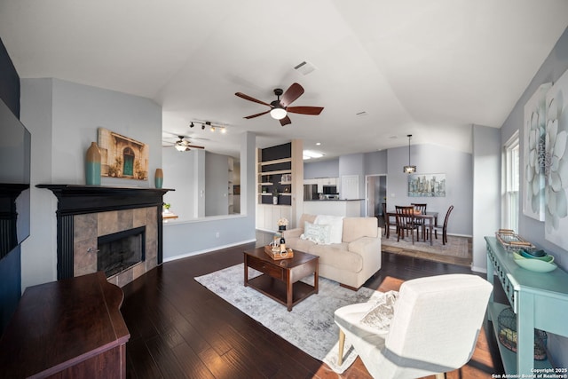 living room featuring ceiling fan, vaulted ceiling, a fireplace, built in features, and dark hardwood / wood-style flooring