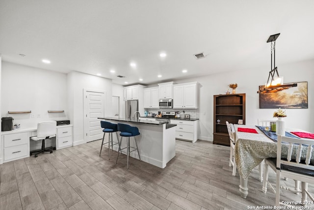 kitchen featuring white cabinets, stainless steel appliances, a kitchen island with sink, and light hardwood / wood-style floors