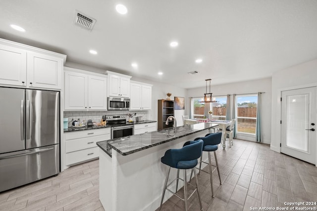 kitchen with hanging light fixtures, white cabinetry, a kitchen island with sink, and appliances with stainless steel finishes