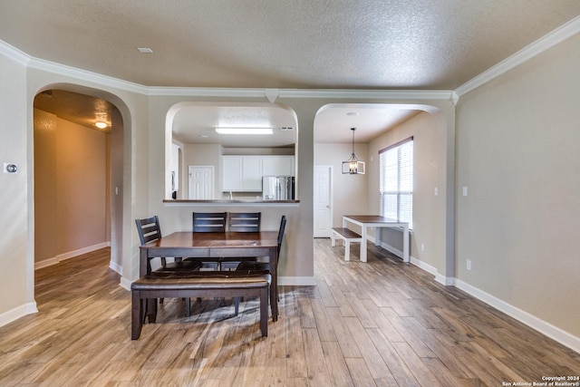 dining area featuring light wood-type flooring, a textured ceiling, and ornamental molding