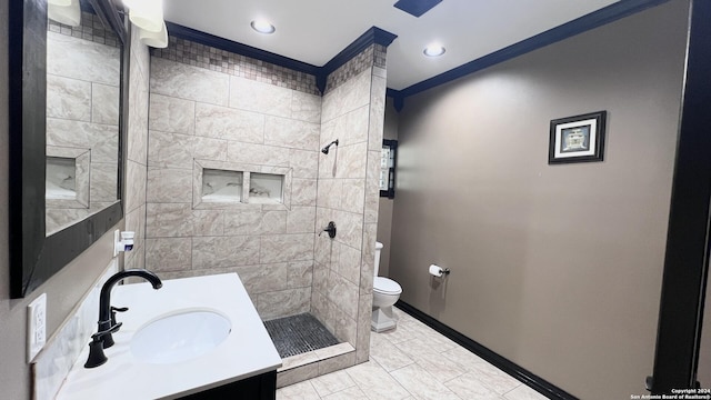 bathroom with vanity, toilet, ornamental molding, and a tile shower