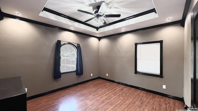 empty room with wood-type flooring, a tray ceiling, ceiling fan, and crown molding