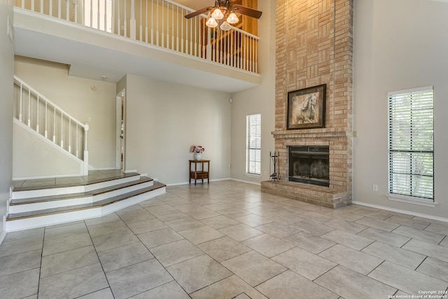 unfurnished living room with ceiling fan, light tile patterned floors, a high ceiling, and a brick fireplace