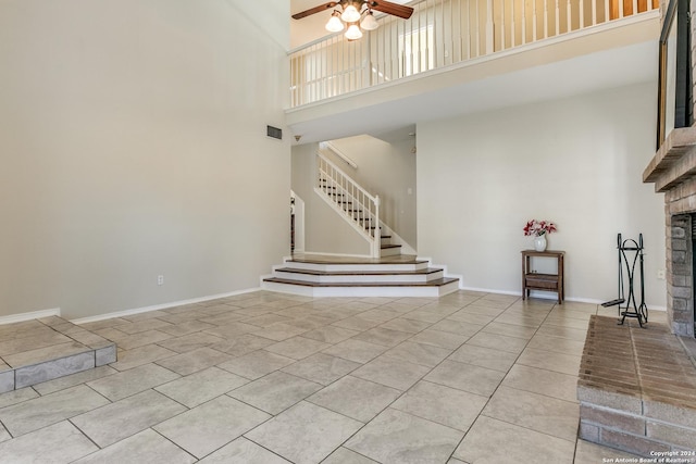 unfurnished living room featuring a fireplace, a high ceiling, light tile patterned floors, and ceiling fan