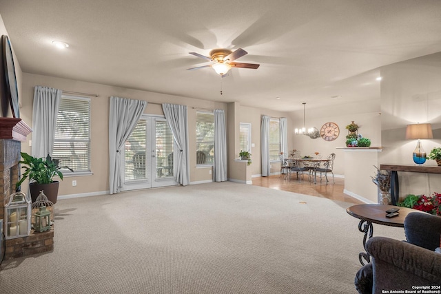 carpeted living room featuring ceiling fan with notable chandelier and a brick fireplace