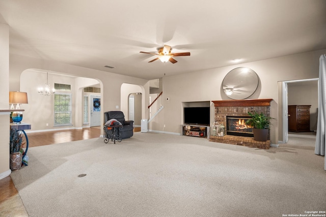 carpeted living room with ceiling fan with notable chandelier and a brick fireplace